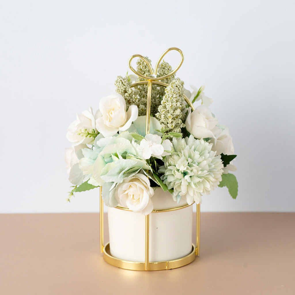 Decorative flower arrangement in a gold holder on a beige surface with a light gray background
