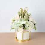 Decorative flower arrangement in a gold holder on a beige surface with a light gray background