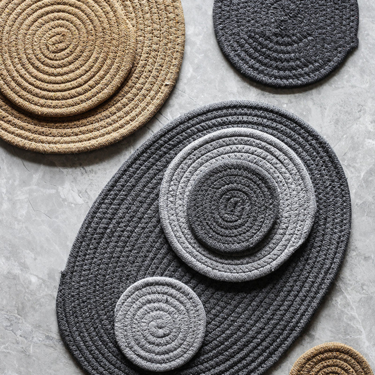 Set of round woven coasters in gray, beige, and black on a concrete surface.