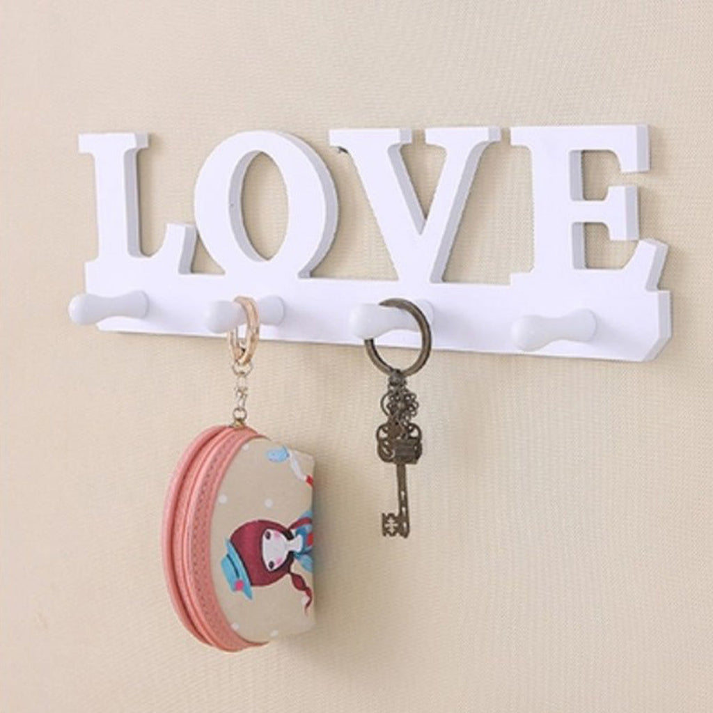 Decorative wall hook with 'LOVE' letters holding keys and a small container on a beige background