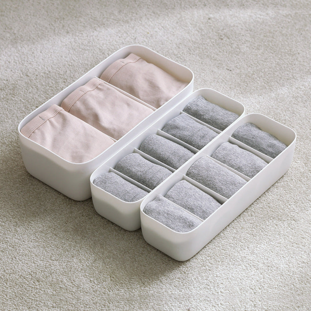 White organizer with compartments containing pink and gray underwear on a light gray background