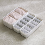 White organizer with compartments containing pink and gray underwear on a light gray background