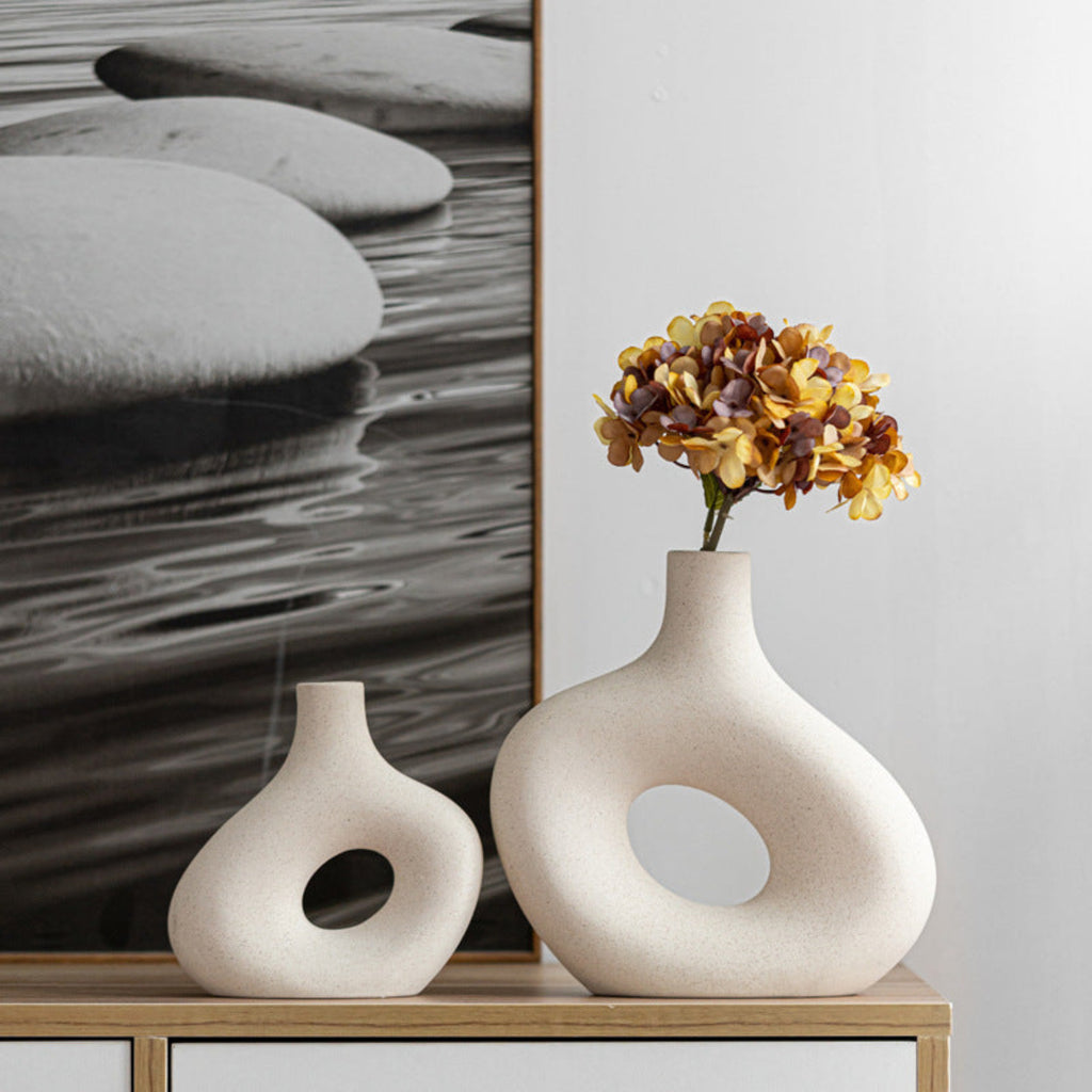 Two ceramic vases on a wooden surface with a piece of abstract art in the background.