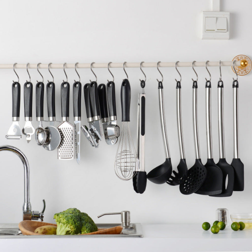 Set of kitchen utensils hanging on a rack above a kitchen counter with vegetables.