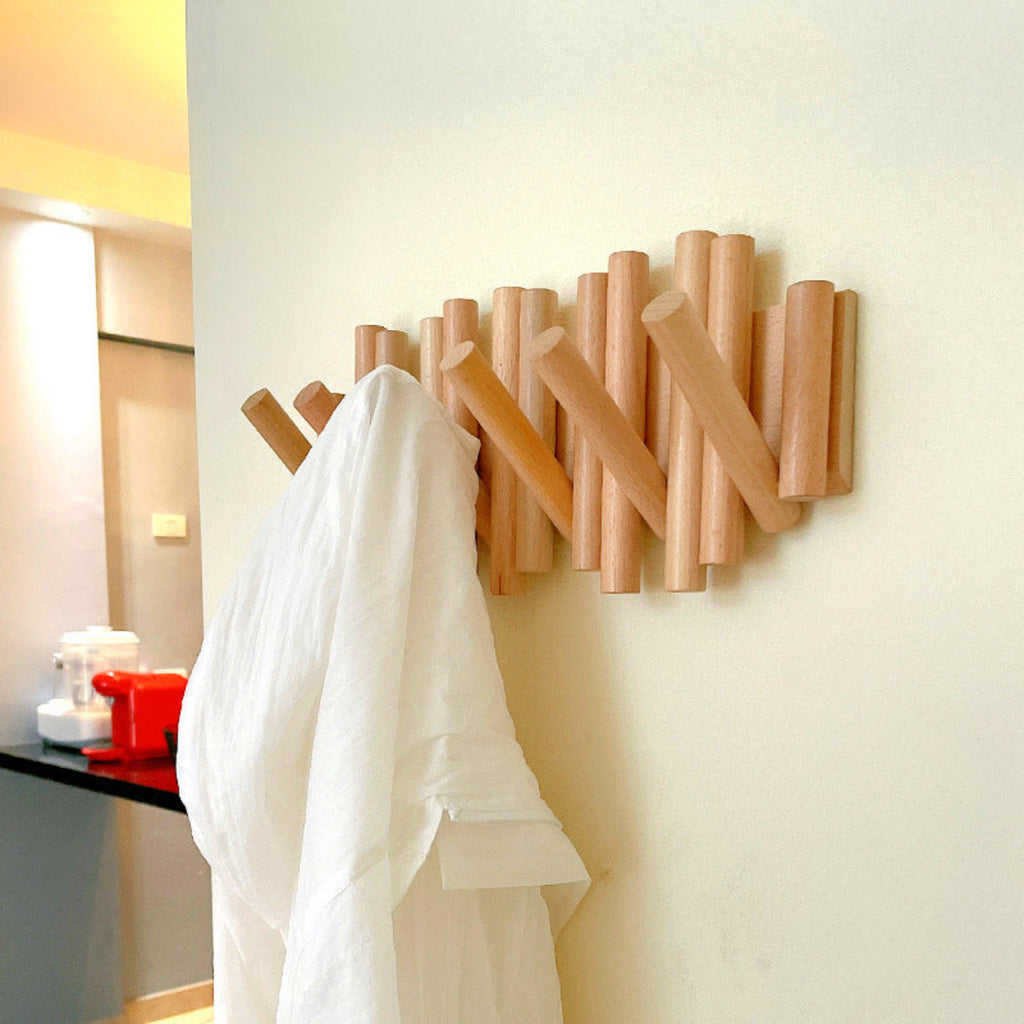 Wooden wall-mounted coat rack with a white garment hanging on it against a light-colored wall.