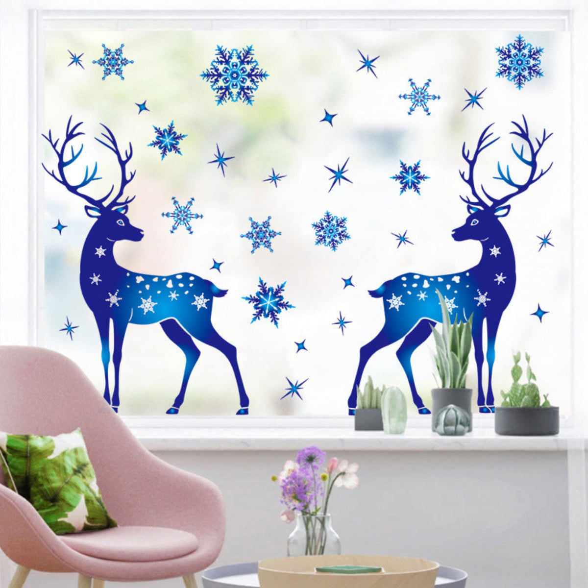 Decorative window stickers of blue deer and snowflakes on a glass pane with a pink chair and plants in the foreground.